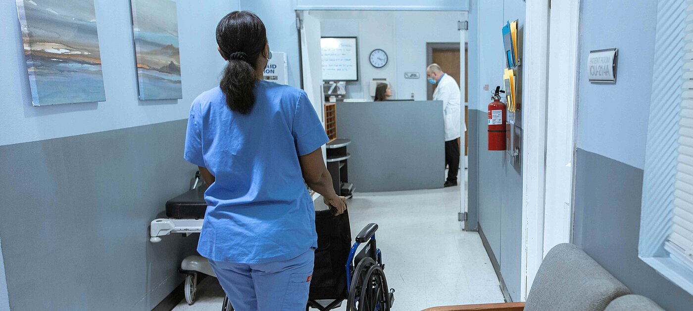 Frau schiebt leeren Rollstuhl im Krankenhaus