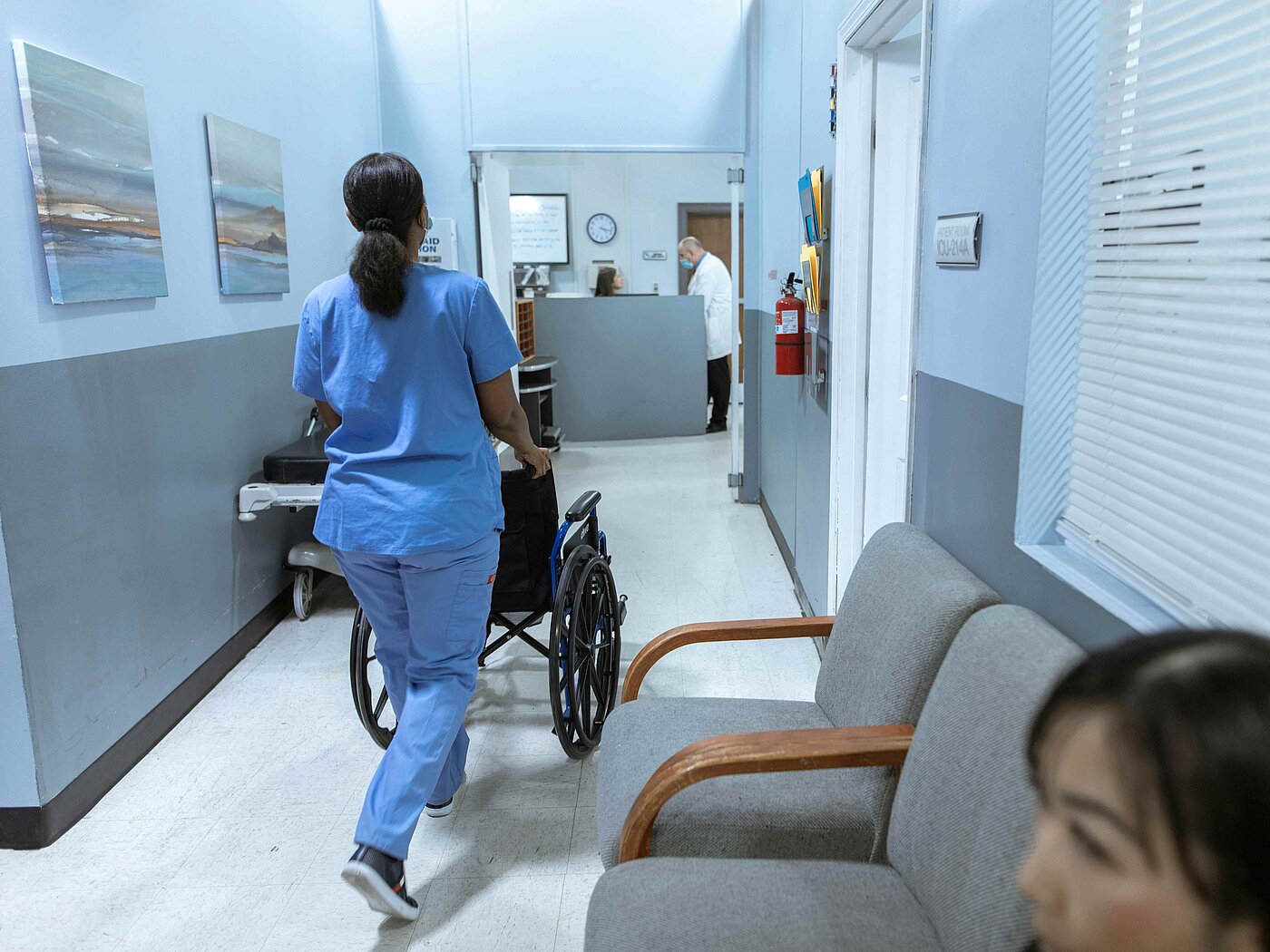 Frau schiebt leeren Rollstuhl im Krankenhaus
